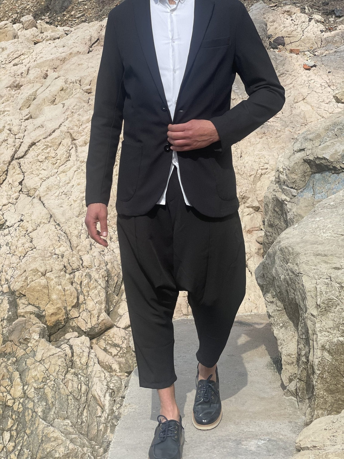 Homme en blazer noir et sarouel sur les rochers, histoire du sarouel